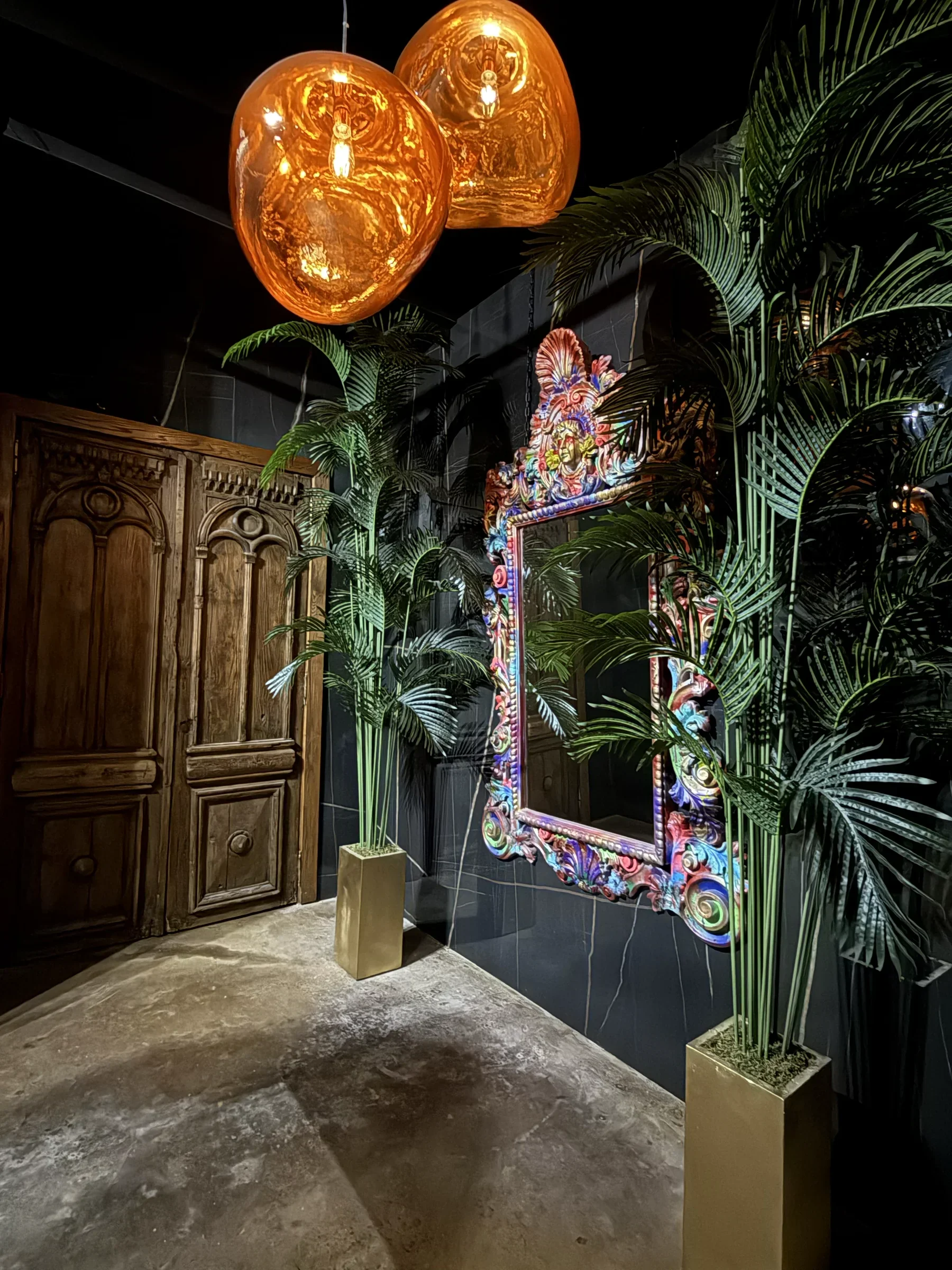 An ornate art frame between palms and copper lamps in the ground-floor bar at Styx + Stone