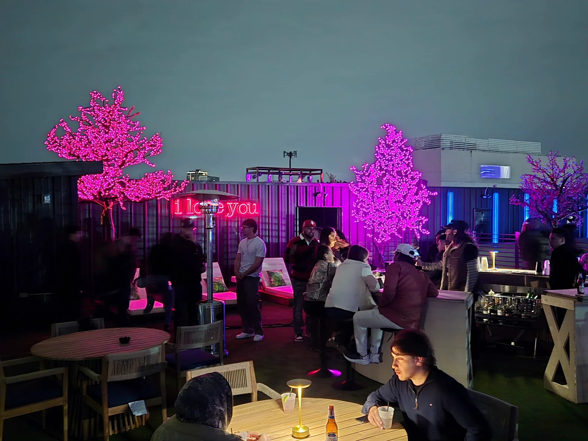 Guests at tables under pink LED trees on the Styx + Stone rooftop at night